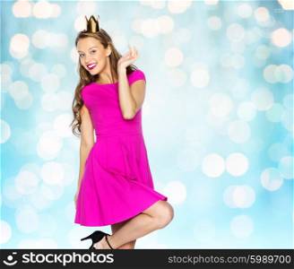 people, holidays and fashion concept - happy young woman or teen girl in pink dress and princess crown over blue holidays lights background
