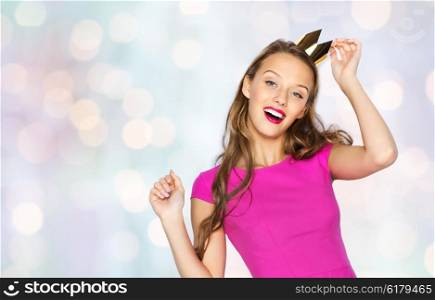 people, holidays and fashion concept - happy young woman or teen girl in pink dress and princess crown over holidays lights background