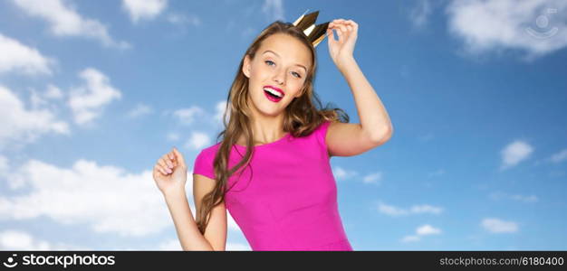 people, holidays and fashion concept - happy young woman or teen girl in pink dress and princess crown over blue sky and clouds background
