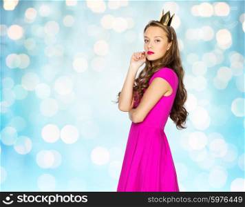 people, holidays and fashion concept - young woman or teen girl in pink dress and princess crown over blue holidays lights background