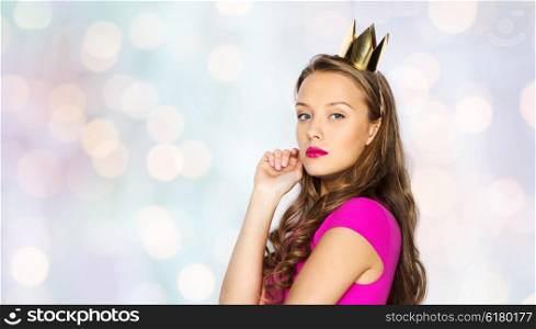 people, holidays and fashion concept - young woman or teen girl in pink dress and princess crown over holidays lights background
