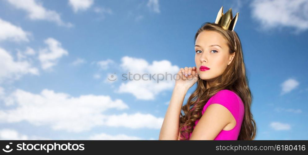 people, holidays and fashion concept - young woman or teen girl in pink dress and princess crown over blue sky and clouds background