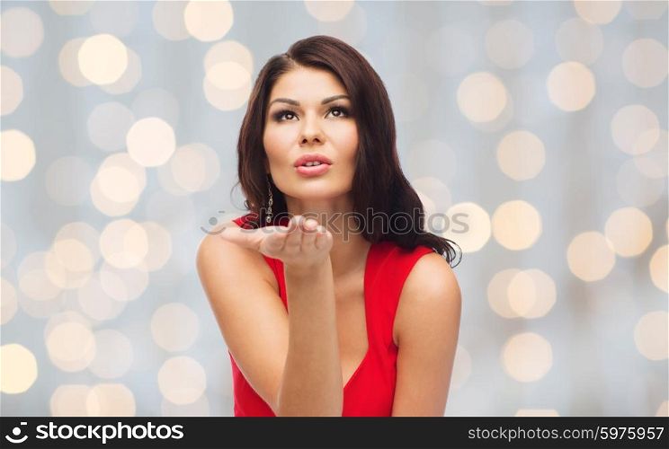 people, holidays and gesture concept - beautiful sexy woman in red dress sending blow kiss over holidays lights background
