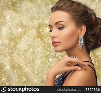 people, holidays and glamour concept - beautiful woman in evening dress wearing ring and earrings over yellow lights background