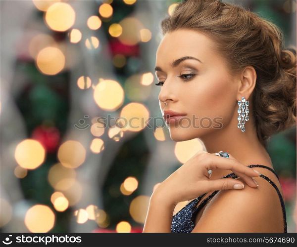 people, holidays and glamour concept - beautiful woman in evening dress wearing ring and earrings over christmas lights background