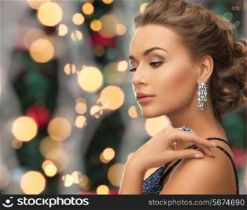 people, holidays and glamour concept - beautiful woman in evening dress wearing ring and earrings over christmas lights background