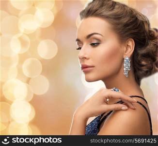people, holidays and glamour concept - beautiful woman in evening dress wearing ring and earrings over beige lights background
