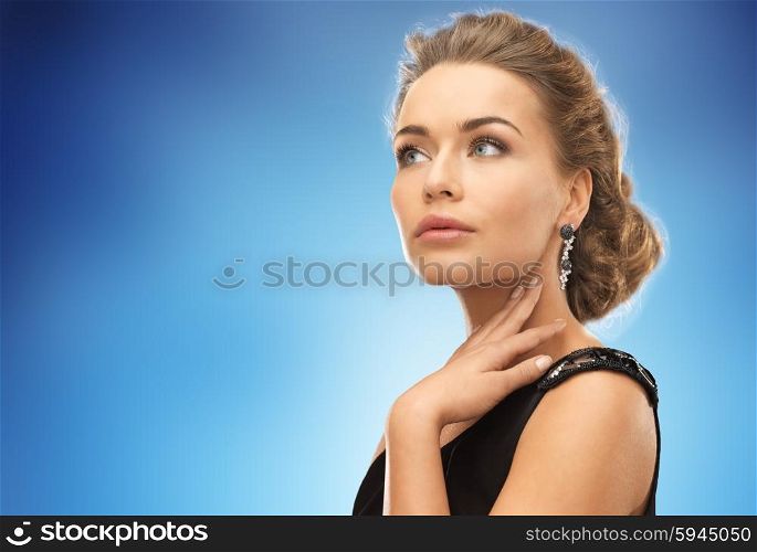 people, holidays and glamour concept - beautiful woman wearing earrings over blue background