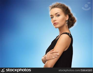 people, holidays and glamour concept - beautiful woman wearing earrings over blue background