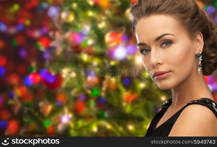 people, holidays and glamour concept - beautiful woman wearing earrings over christmas lights background