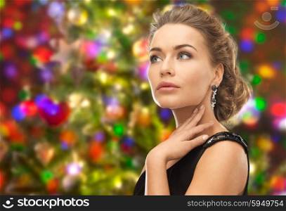 people, holidays and glamour concept - beautiful woman wearing earrings over christmas lights background