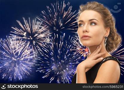 people, holidays and glamour concept - beautiful woman wearing earrings over firework on dark blue background