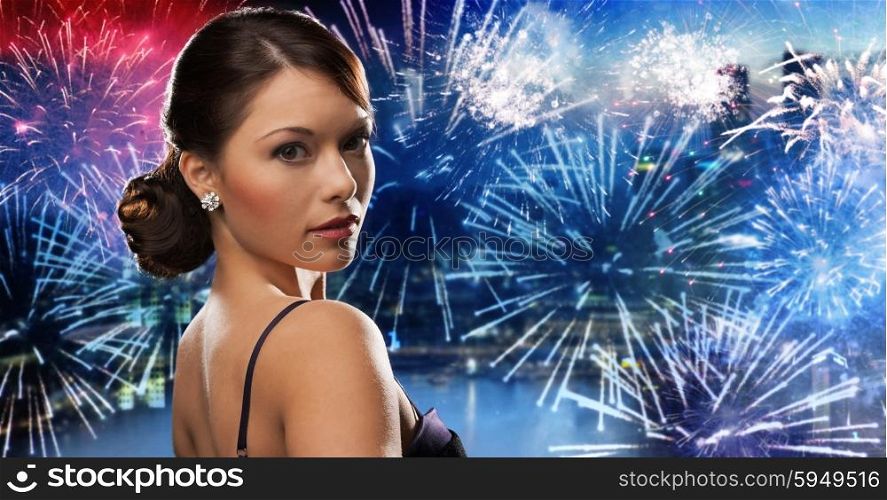 people, holidays and glamour concept - beautiful woman with diamond earring over nigh city and firework background