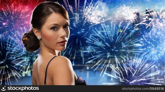 people, holidays and glamour concept - beautiful woman with diamond earring over nigh city and firework background