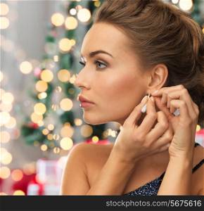 people, holidays and glamour concept - close up of beautiful woman wearing earrings over christmas tree and lights background