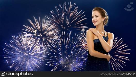 people, holidays and glamour concept - happy beautiful woman in evening dress over firework on dark blue background