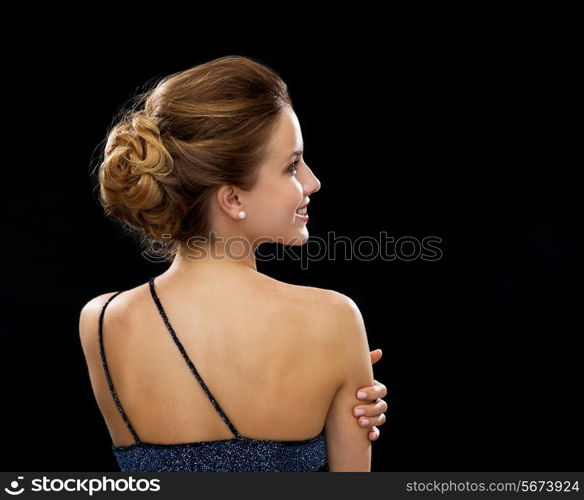 people, holidays and glamour concept - smiling woman in evening dress from the back over black background