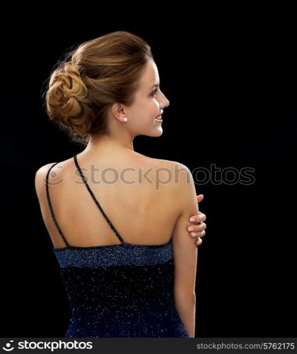 people, holidays and glamour concept - smiling woman in evening dress from the back over black background