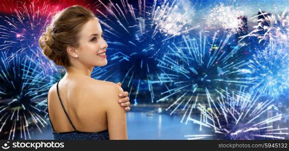 people, holidays and glamour concept - smiling woman in evening dress from back over nigh city and firework background