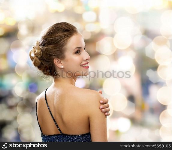 people, holidays and glamour concept - smiling woman in evening dress over black background over lights background from back