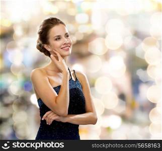 people, holidays and glamour concept - smiling woman in evening dress over black background over lights background