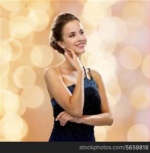 people, holidays and glamour concept - smiling woman in evening dress over black background over beige lights background