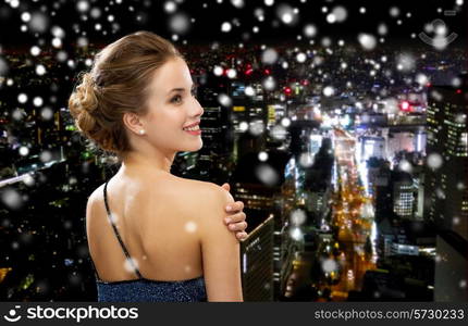 people, holidays and glamour concept - smiling woman in evening dress over black background over snowy night city background from back