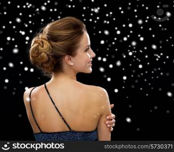 people, holidays and glamour concept - smiling woman in evening dress over black snowy background from back