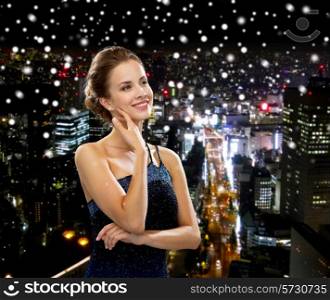 people, holidays and glamour concept - smiling woman in evening dress over black background over snowy night city background