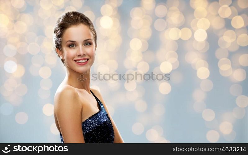 people, holidays and glamour concept - smiling woman in evening dress over lights background