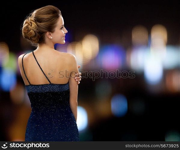 people, holidays and glamour concept - smiling woman in evening dress over night lights background