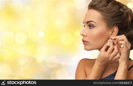 people, holidays and glamour concept - smiling woman in evening dress wearing earrings over yellow lights background