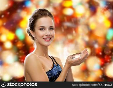 people, holidays and glamour concept - smiling woman in evening dress with diamond over red lights background
