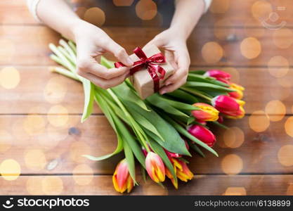 people, holidays and greeting concept - close up of woman holding gift box and tulip flowers over holidays lights