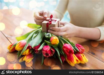 people, holidays and greeting concept - close up of woman holding gift box and tulip flowers over lights