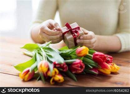 people, holidays and greeting concept - close up of woman holding gift box and tulip flowers