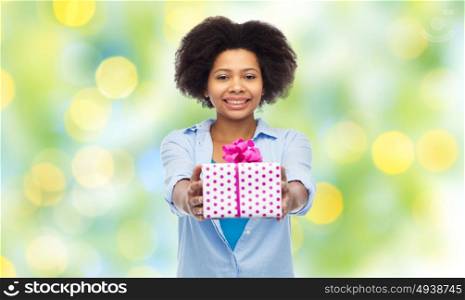 people, holidays and greeting concept - happy african american young woman with birthday gift box over summer green lights background. happy african woman with birthday gift box