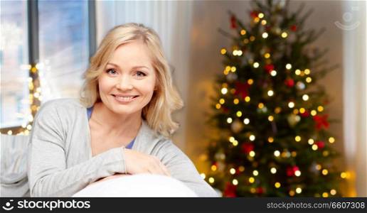 people, holidays and leisure concept - happy middle aged woman at home over christmas tree lights background. happy middle aged woman at home on christmas