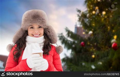 people, holidays and leisure concept - happy woman in winter fur with coffee cup hat over christmas tree at tallinn old town hall square background. woman with coffee over christmas tree in tallinn