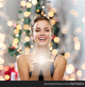 people, holidays and magic concept - laughing woman in evening dress holding something over christmas tree and lights background
