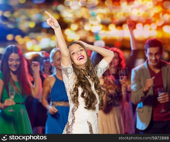 people, holidays and nightlife concept - happy young woman or teen girl in fancy dress with sequins and long wavy hair dancing at night club party over crowd and lights background