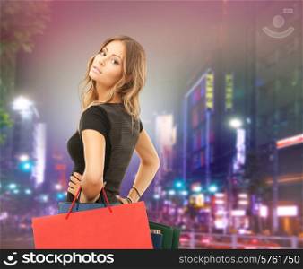 people, holidays and sale concept - young happy woman with shopping bags over night city street background