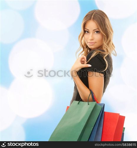 people, holidays and sale concept - young happy woman with shopping bags over blue lights background