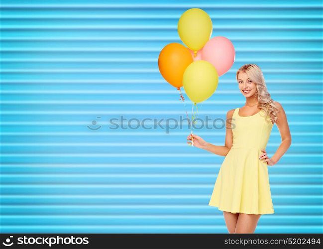 people, holidays and summer party concept - happy young woman or teen girl in yellow dress with helium air balloons over ribbed blue background. happy woman in dress with helium air balloons