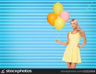 people, holidays and summer party concept - happy young woman or teen girl in yellow dress with helium air balloons over ribbed blue background. happy woman in dress with helium air balloons
