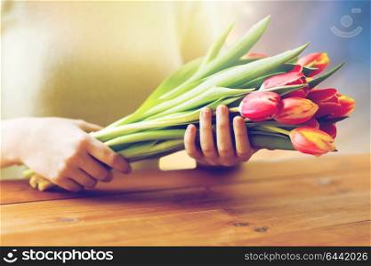 people, holidays and womens day concept - close up of woman holding tulip flowers above wooden table. close up of woman holding tulip flowers