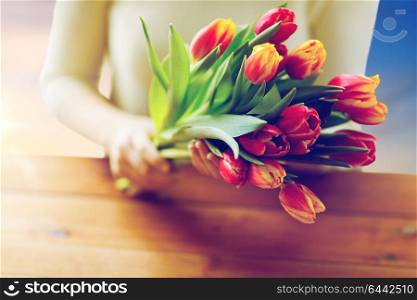 people, holidays and womens day concept - close up of woman holding tulip flowers above wooden table. close up of woman holding tulip flowers