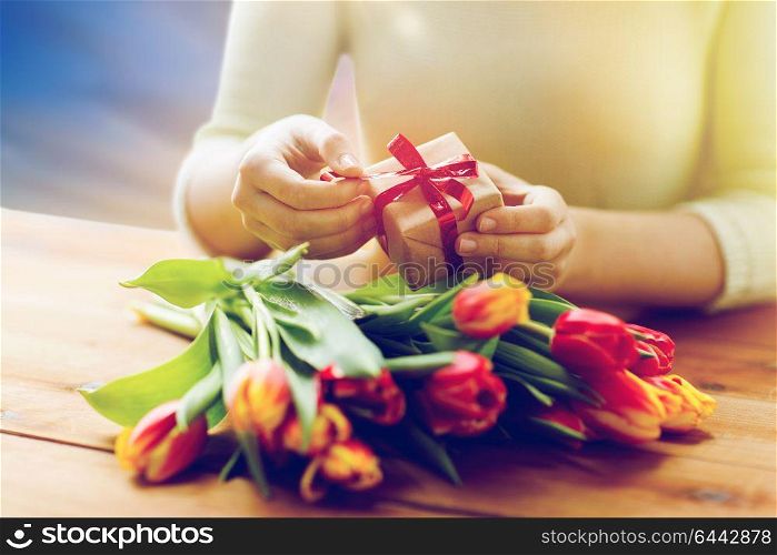 people, holidays and womens day concept - close up of woman holding gift box and tulip flowers on table. close up of woman with gift box and tulip flowers