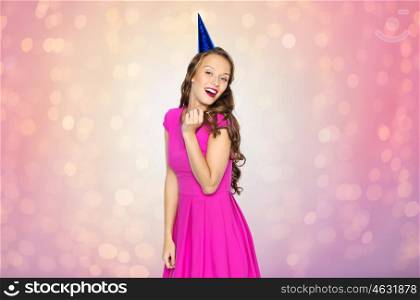 people, holidays, birthday and celebration concept - happy young woman or teen girl in pink dress and party cap over rose quartz and serenity lights background