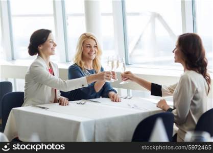people, holidays, celebration and lifestyle concept - happy women drinking champagne and clinking glasses at restaurant
